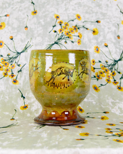 Green ceramic cup with a deer design on a floral-patterned background