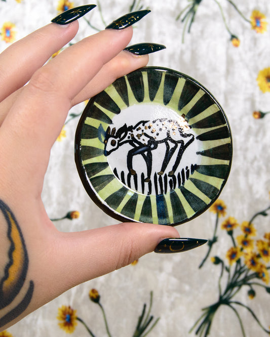 Hand holding a round ceramic coaster with a deer design against a floral background