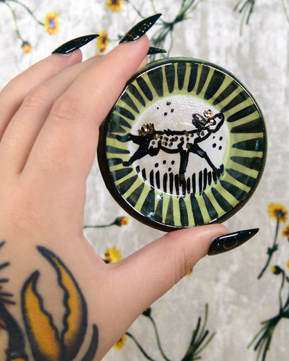 Hand holding a decorative plate with a black and white deer design against a floral background