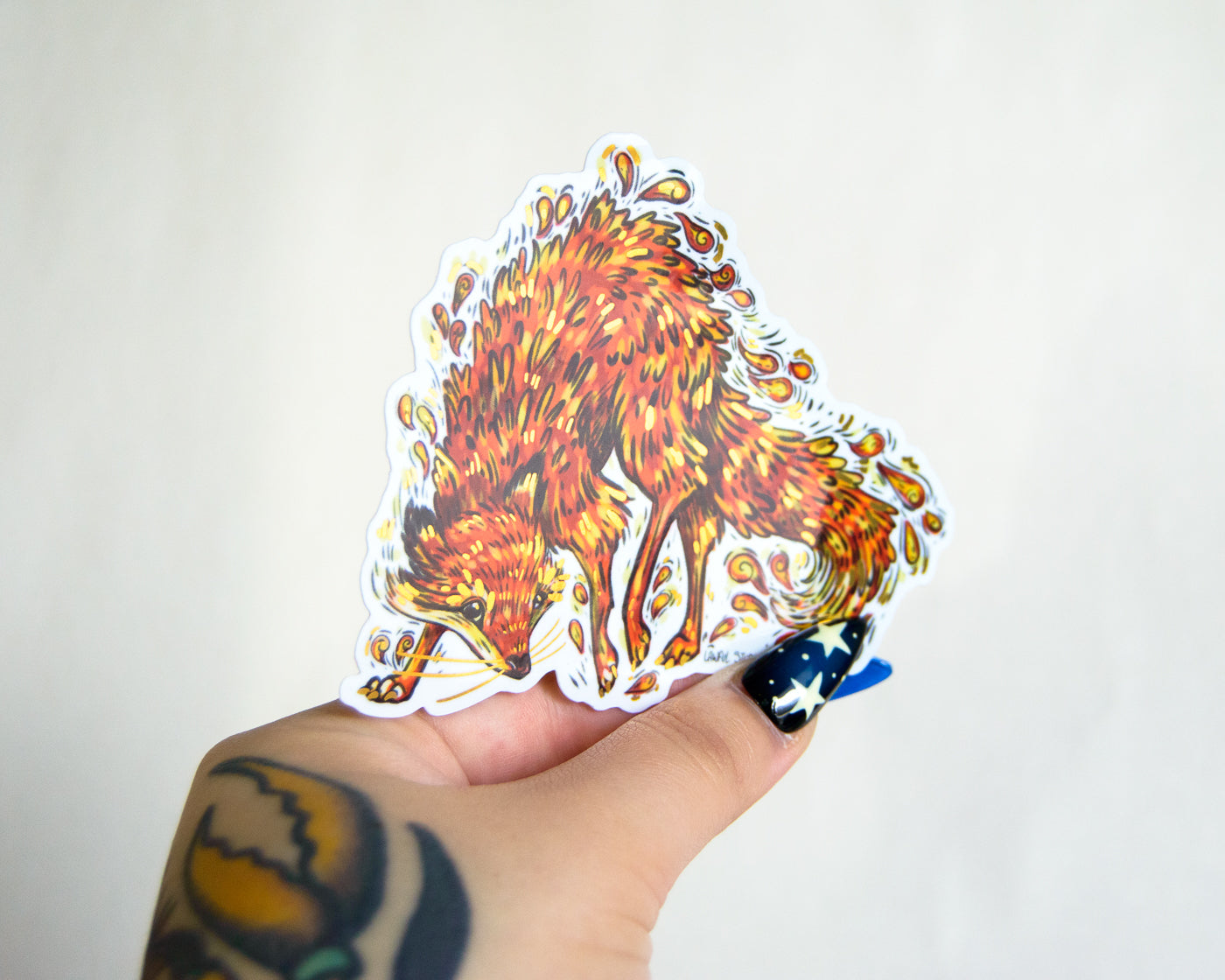 Hand holding a sticker of a fiery fox sticker design against a plain background