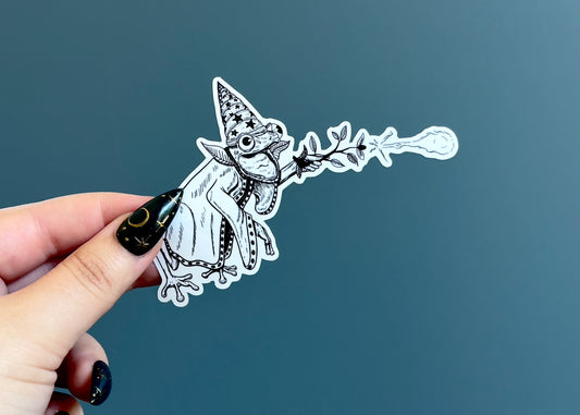 Black and white illustrated sticker of a cute frog  wizard casting a spell 