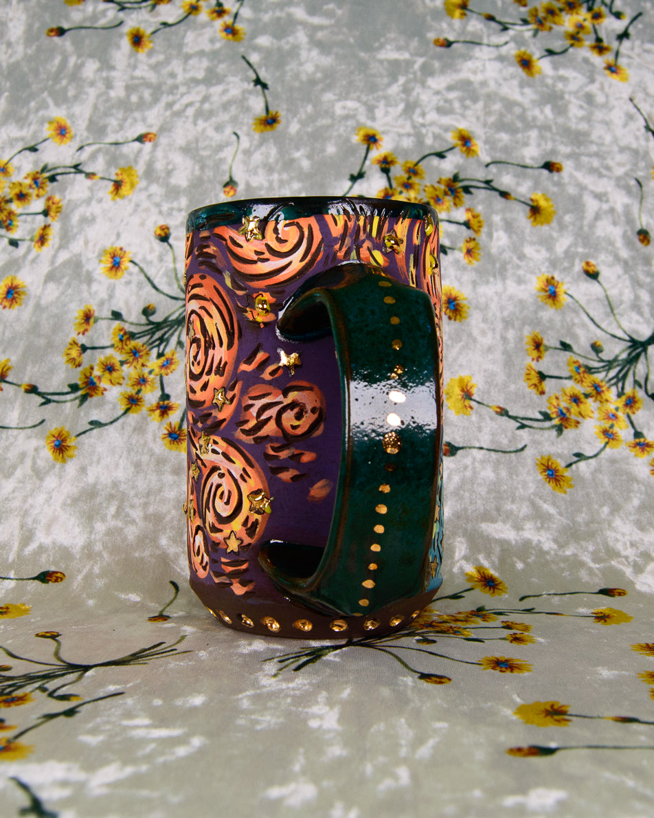 Colorful ceramic stoneware mug with purple and orange artistic designs and a gold and green handle