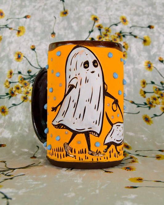 Mug with a ghost design on an orange background, against a floral patterned background.