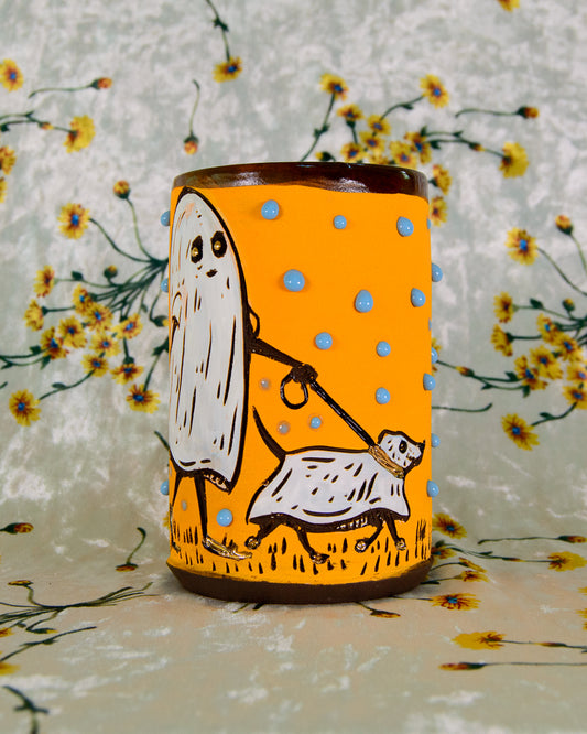 Decorative mug with ghost and dog illustration on a yellow background, against a floral patterned backdrop.