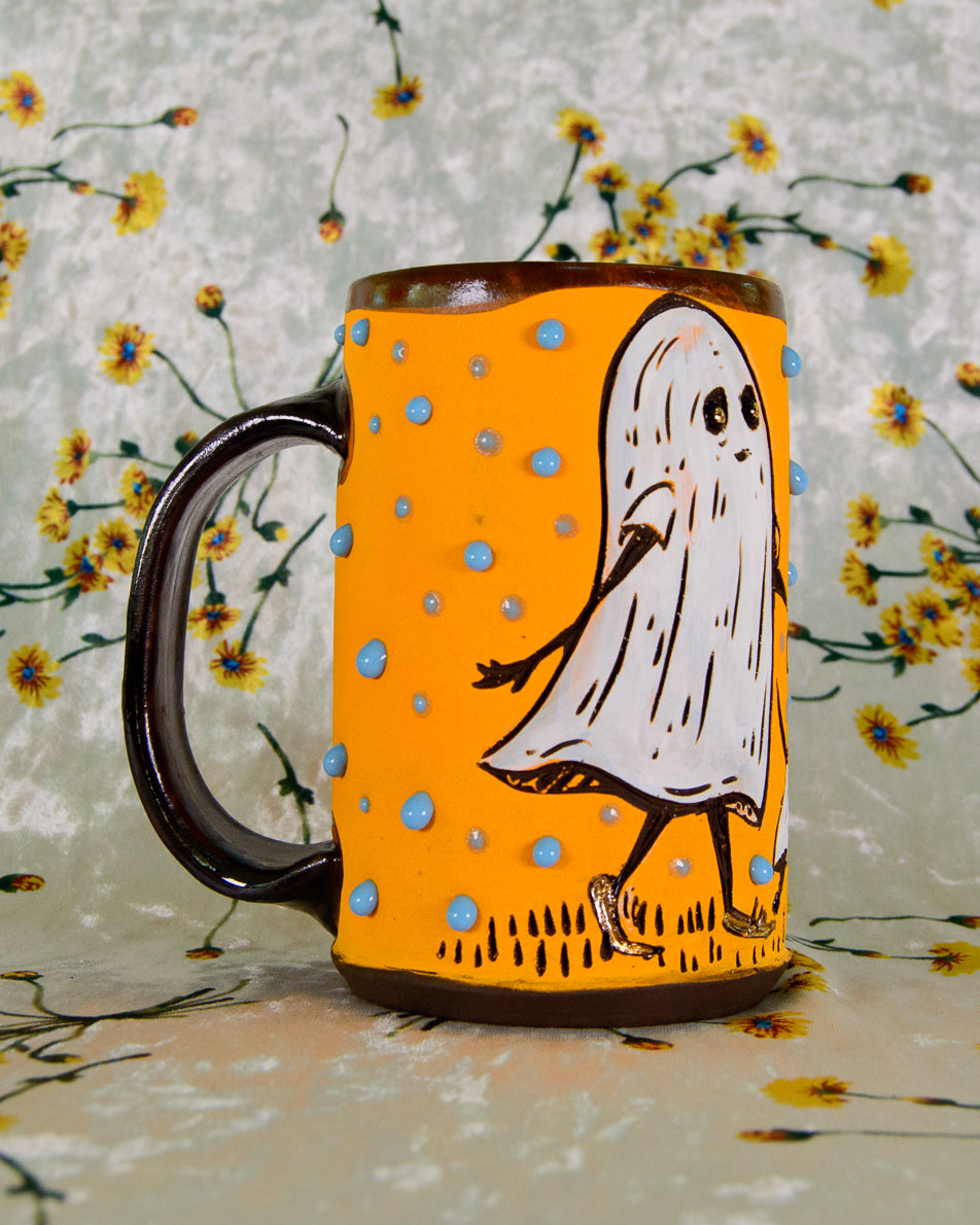 Mug with a ghost design on an orange background against a floral patterned background