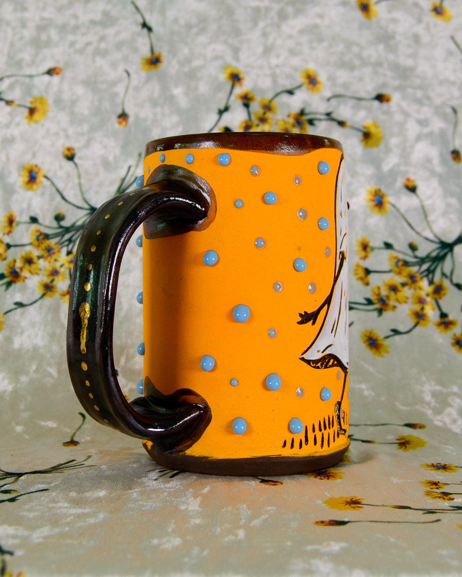 Orange mug with blue polka dots and a black handle on a floral-patterned background