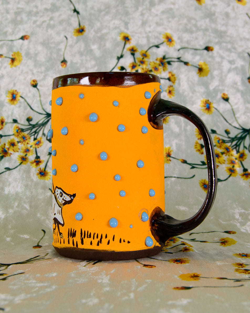 Orange mug with blue polka dots and a brown handle on a floral background