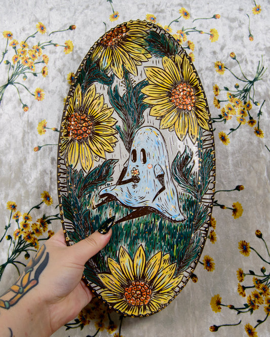 Decorative plate with a ghost design surrounded by yellow flowers, held against a floral background.