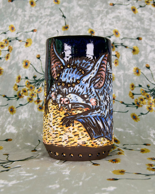 Blue and yellow ceramic mug with a cartoon cute bat design on a pile of gold 