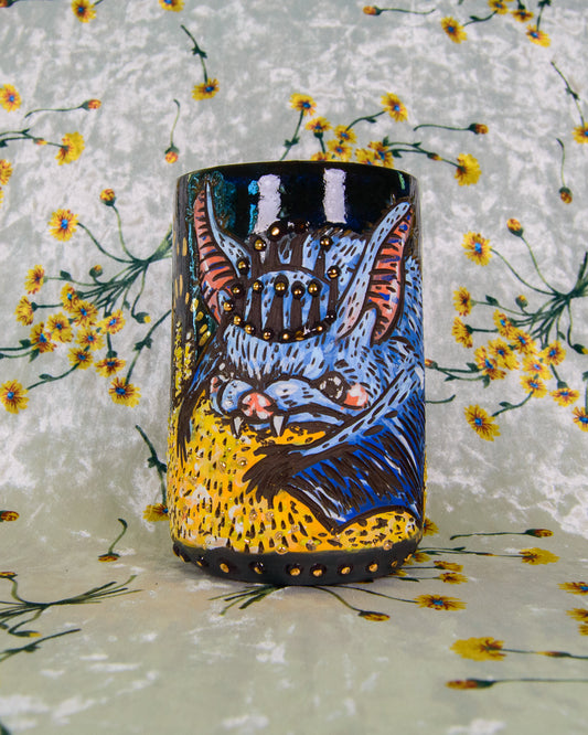 Dark blue mug with a hand painted design of a blue cartoon bat wearing a crown and holding gold coins