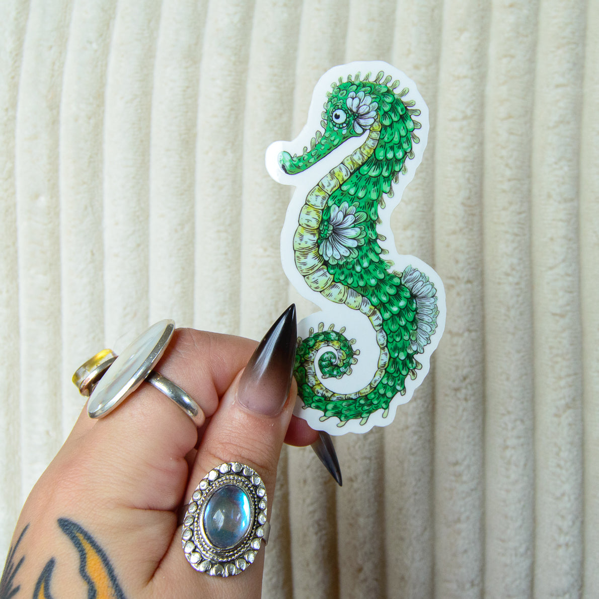 Hand holding a cute decorative green seahorse sticker against a beige background