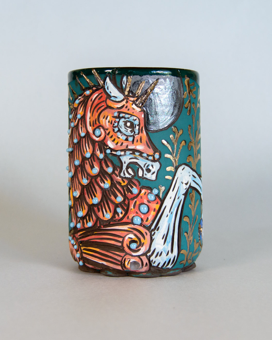 Ceramic mug with a colorful design of an illuminated manuscript style unicorn on a light gray background