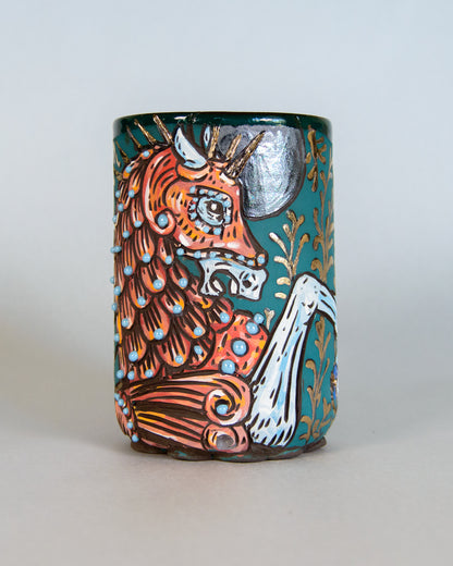 Ceramic mug with a colorful design of an illuminated manuscript style unicorn on a light gray background