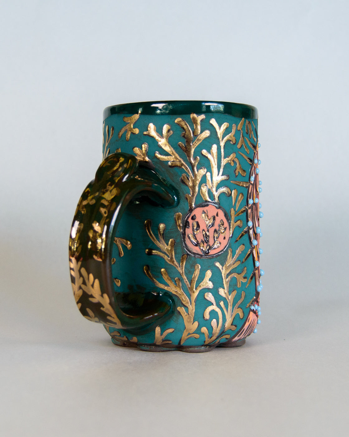 Teal mug with gold and bronze leaf pattern on a white background