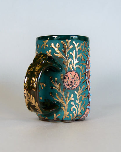 Teal mug with gold and bronze leaf pattern on a white background