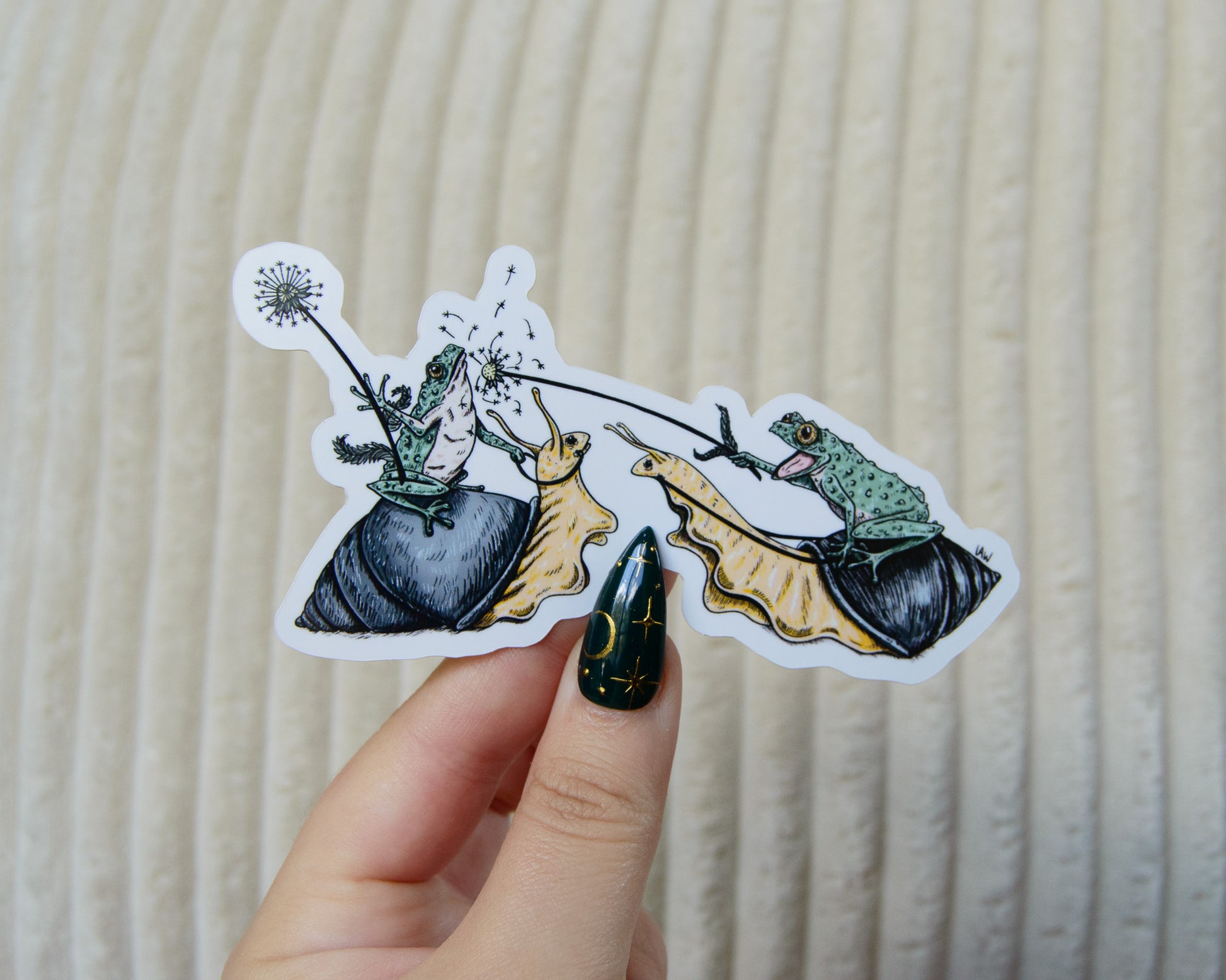 Hand holding a sticker with two frogs riding snails and jousting with dandelions against a beige background