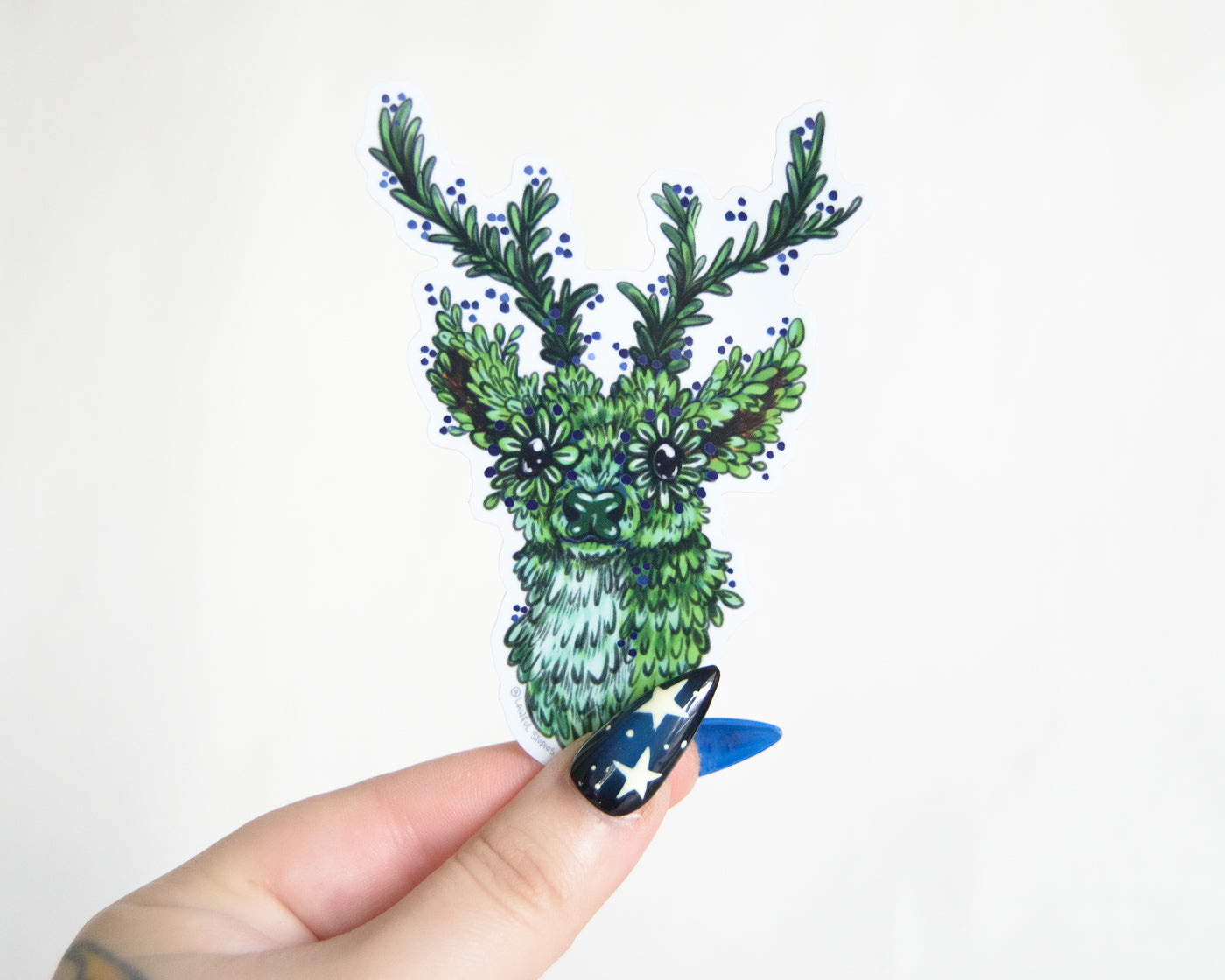 Hand holding a decorative sticker of a green deer with antlers on a white background