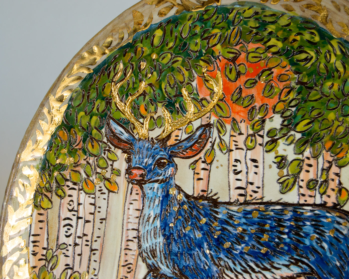 Decorative plate with a blue deer and forest design on a gold rim.