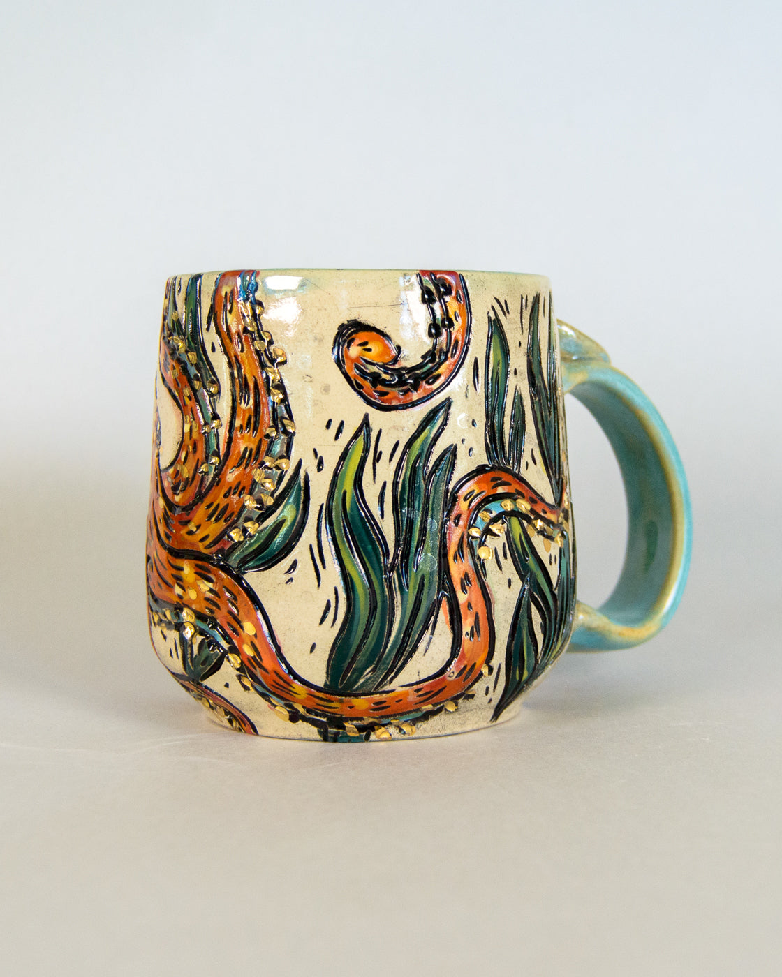 Ceramic mug with artistic octopus design and leaves on a plain background