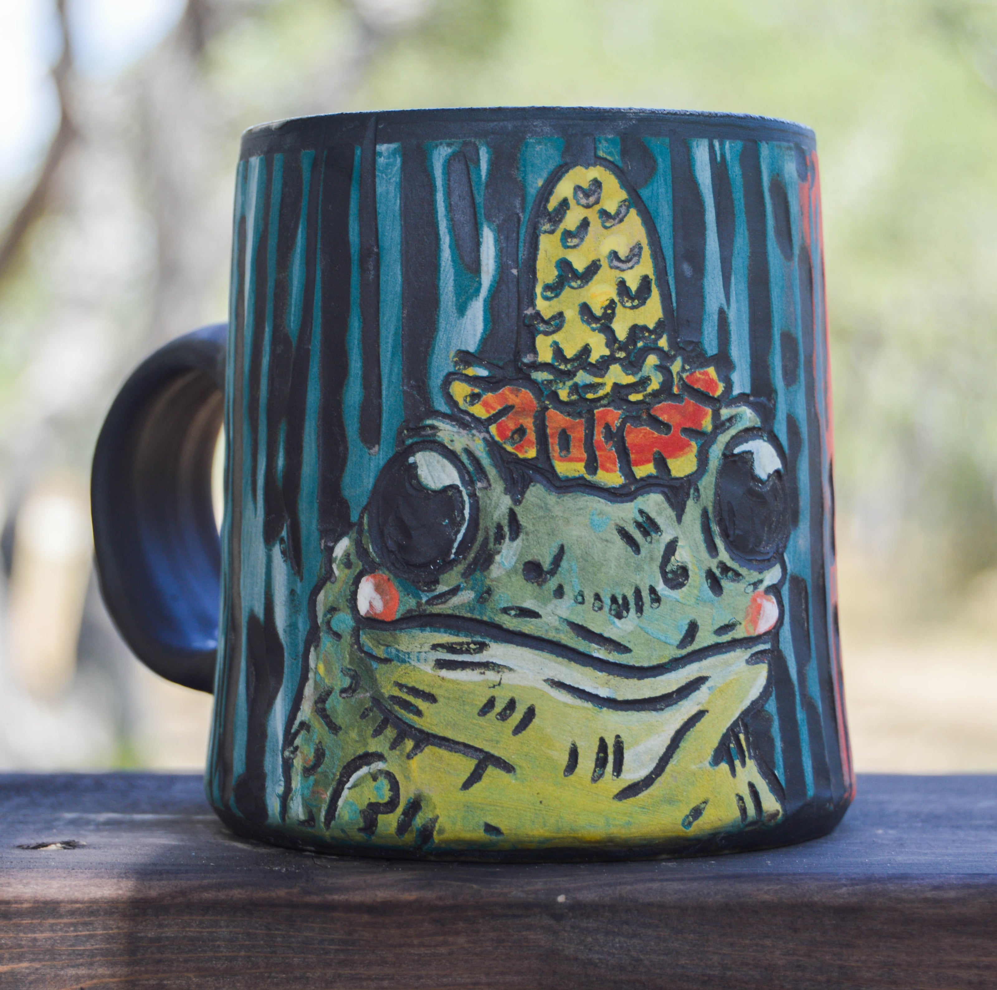 Mug with a frog design wearing a hat on a wooden surface