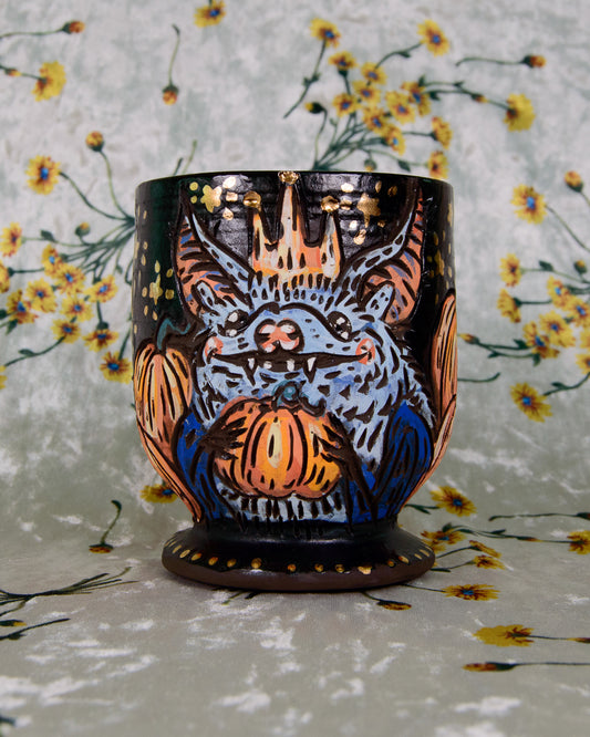 Black matte ceramic stoneware goblet with a blue design of a bat king holding a pumpkin and wearing a crown