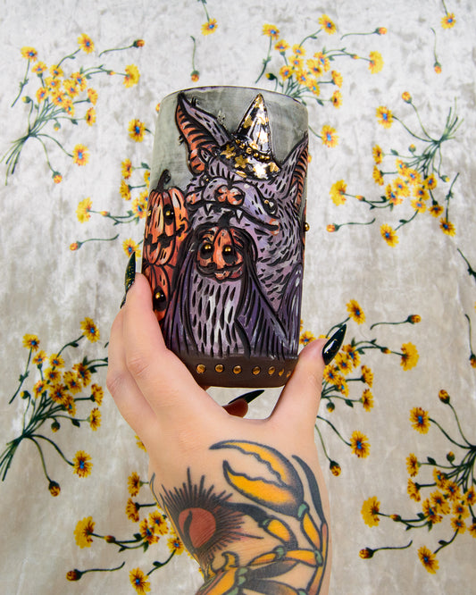 Hand holding an illustrated mug of a cartoon bat with halloween themed pumpkins