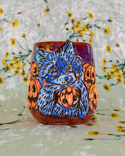 Ceramic wine cup with a blue raccoon holding a pumpkin design on a floral background