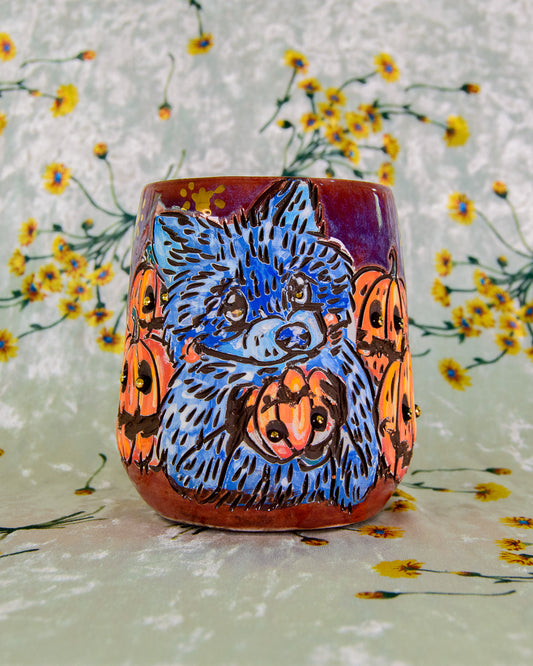 Ceramic wine cup with a blue raccoon holding a pumpkin design on a floral background