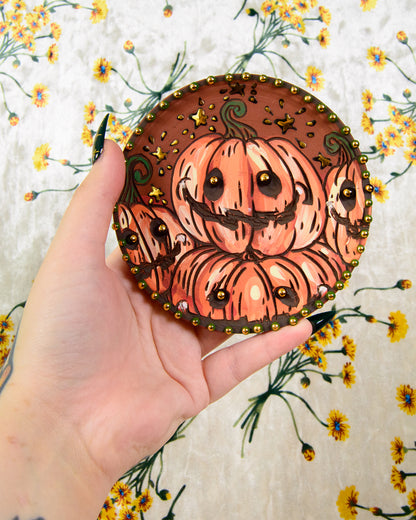 Decorative coaster with pumpkins held by a hand on a floral background
