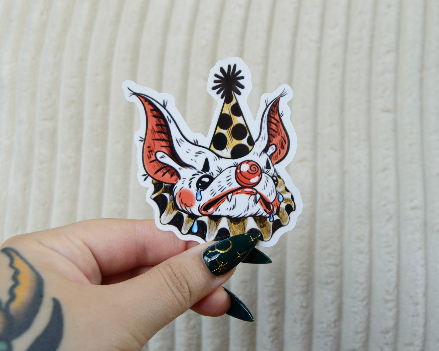 A colorful stylized sticker of a sad clown bat wearing makeup and a pointed hat while crying