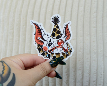 A colorful stylized sticker of a sad clown bat wearing makeup and a pointed hat while crying