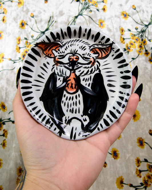 Hand holding a round ceramic plate with a black and white bat design against a floral background