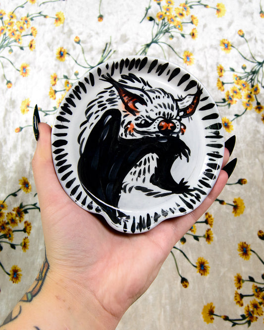 Hand holding a decorative plate with a black and white bat design against a floral background