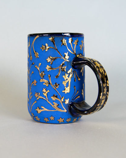 Blue mug with gold floral patterns on a white background