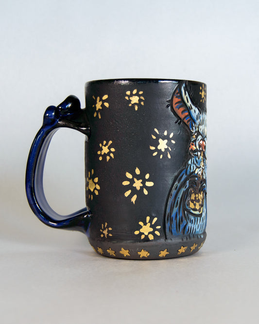 Black mug with blue bat design and gold star patterns on a white background