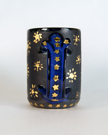 Black mug with blue handle and gold star patterns on a white background