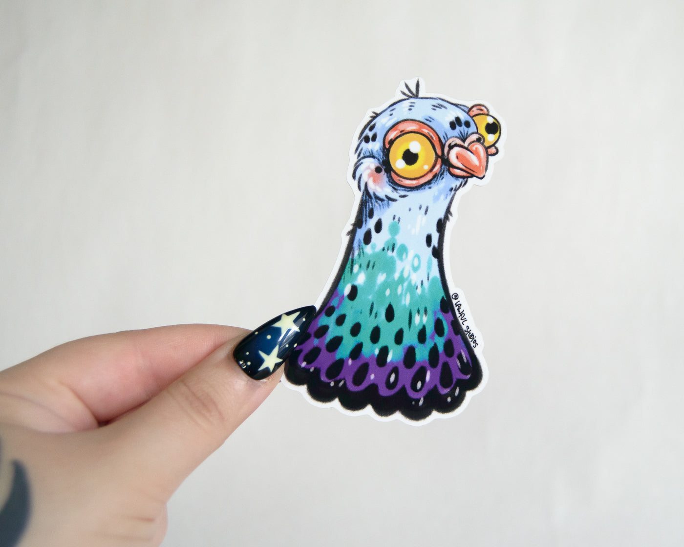 Colorful cartoon-like pigeon sticker held by a hand on a white background