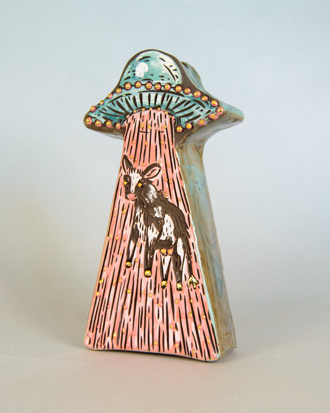 Ceramic vase of a cow inside a stylized UFO on a light gray background