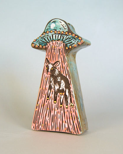 Ceramic vase of a cow inside a stylized UFO on a light gray background
