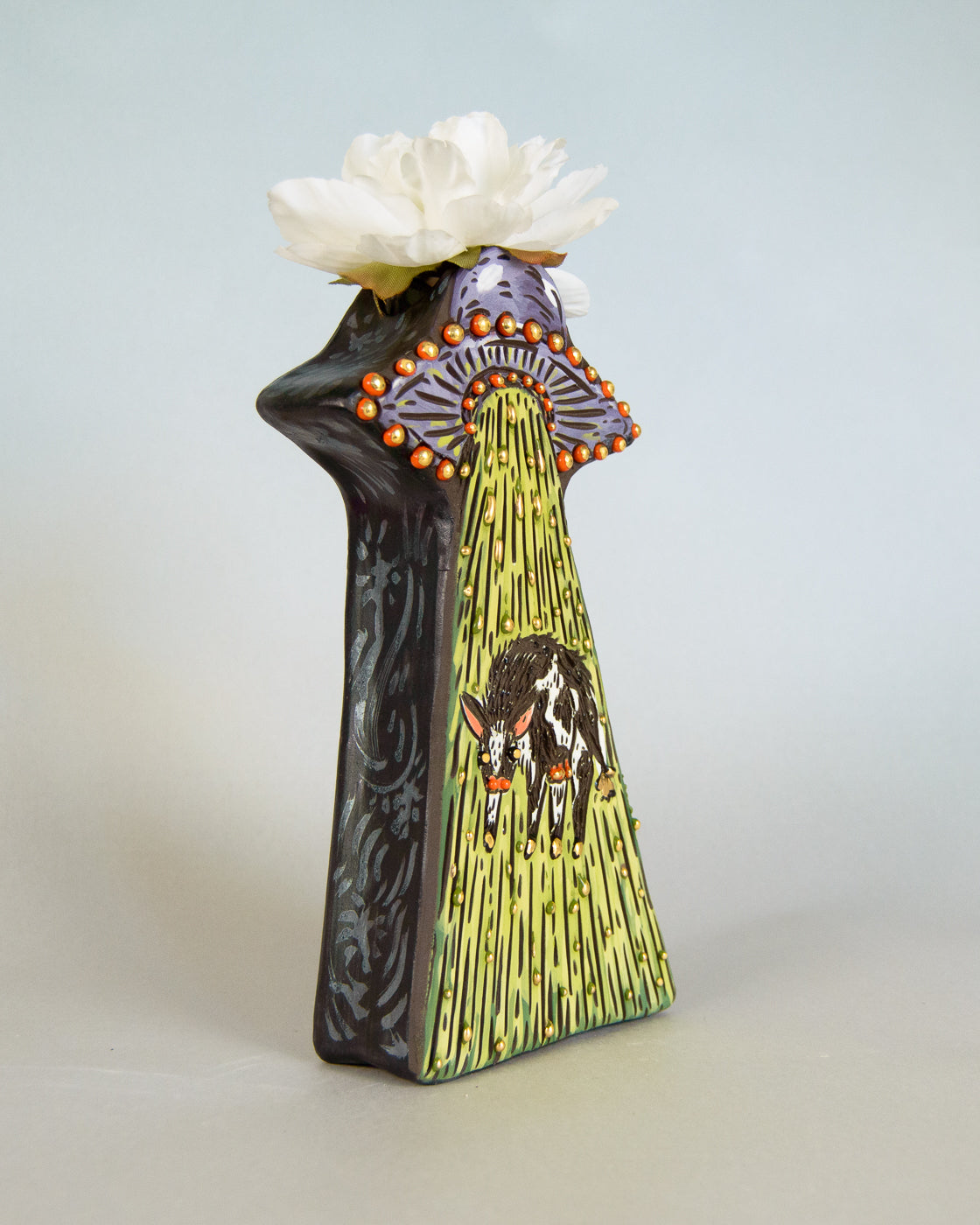 Decorative vase with a design of a cow and ufo and a white flower on top against a light gray background
