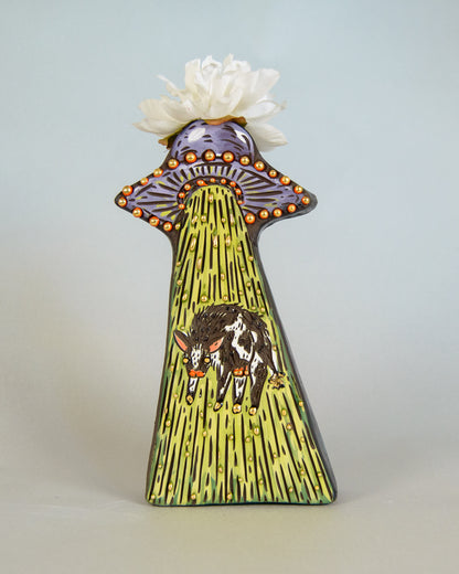 Vase with alien UFO ship and cow design  with a white flower on top against a light gray background
