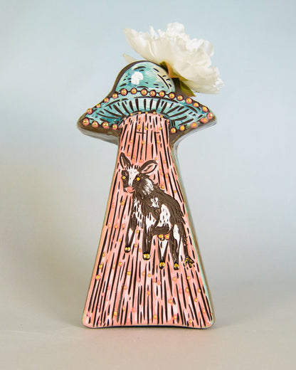 Decorative vase with a design of a cow in a UFO, on a light blue background.