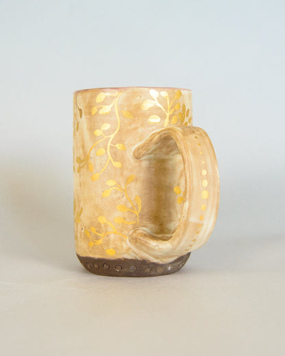Ceramic mug with gold leaf pattern on a light gray background