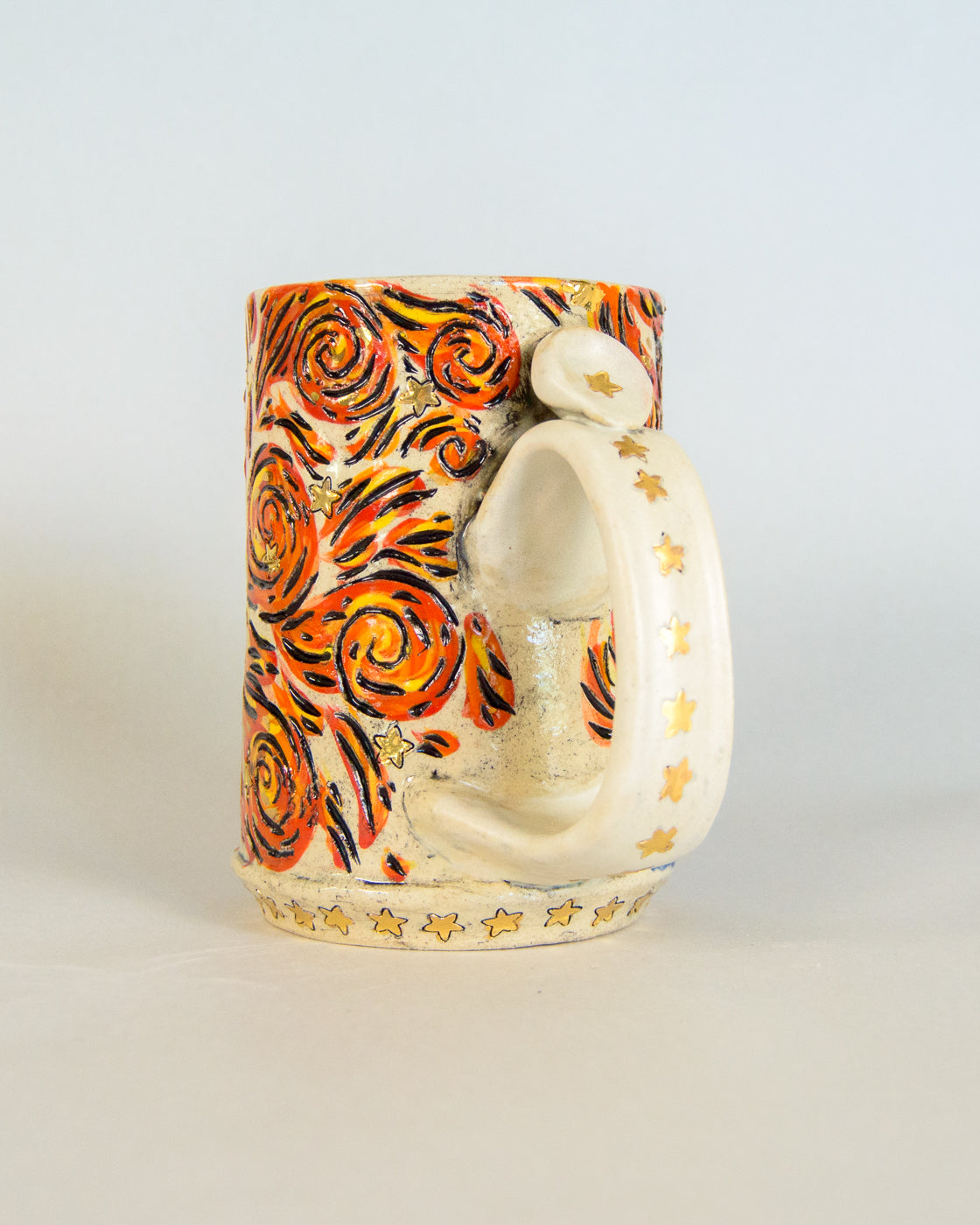 Decorative ceramic mug with orange and black swirl patterns on a light gray background