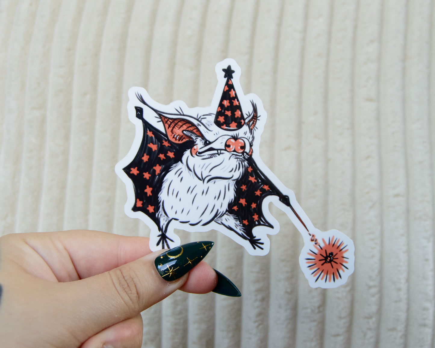 Hand holding a Halloween-themed sticker of a bat wearing a witch wizard hat with a magic wand zapping a spider