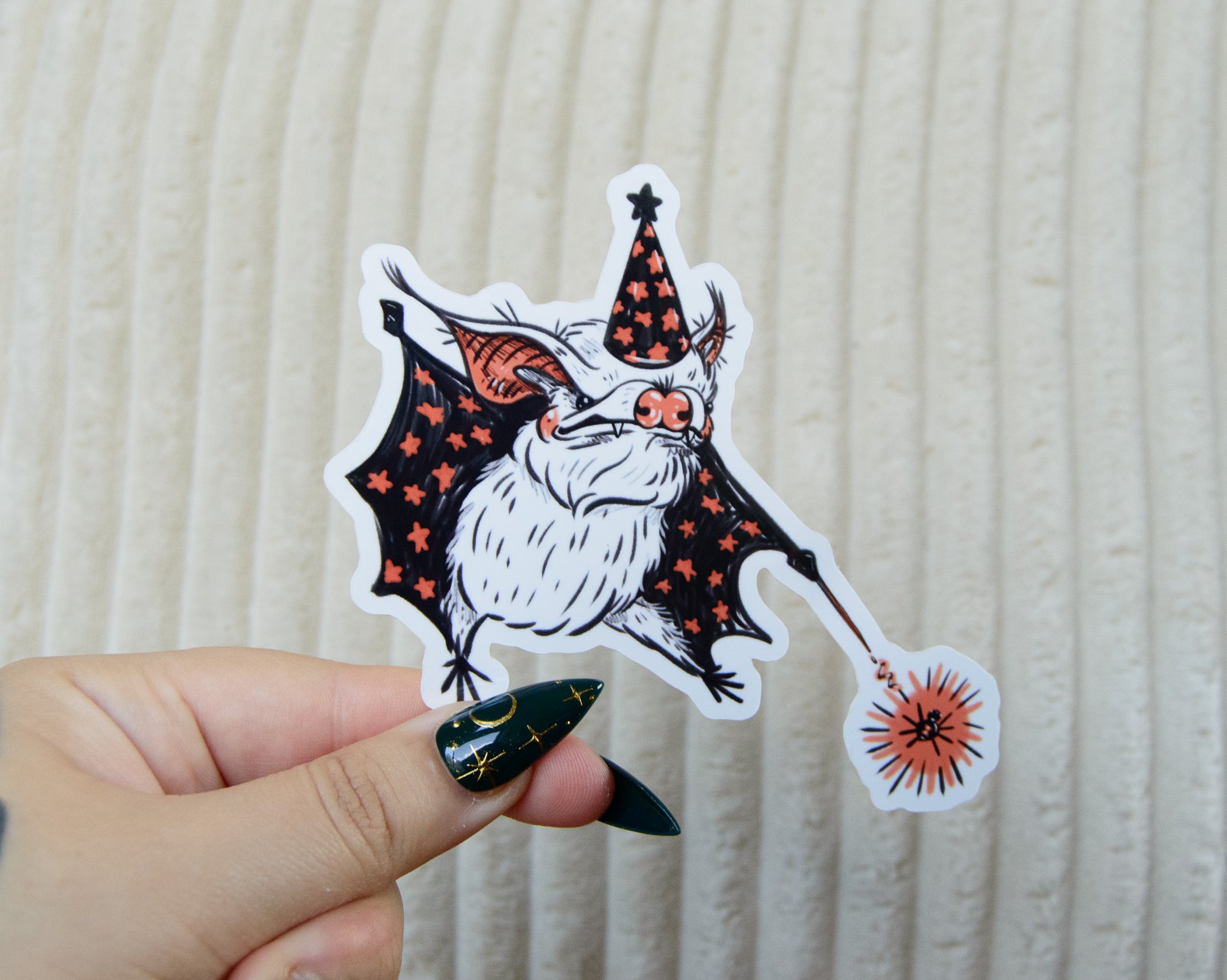 Hand holding a Halloween-themed sticker of a bat wearing a witch wizard hat with a magic wand zapping a spider